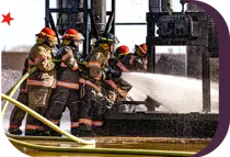 group of firemen in full gear holding a firehouse spraying a fire